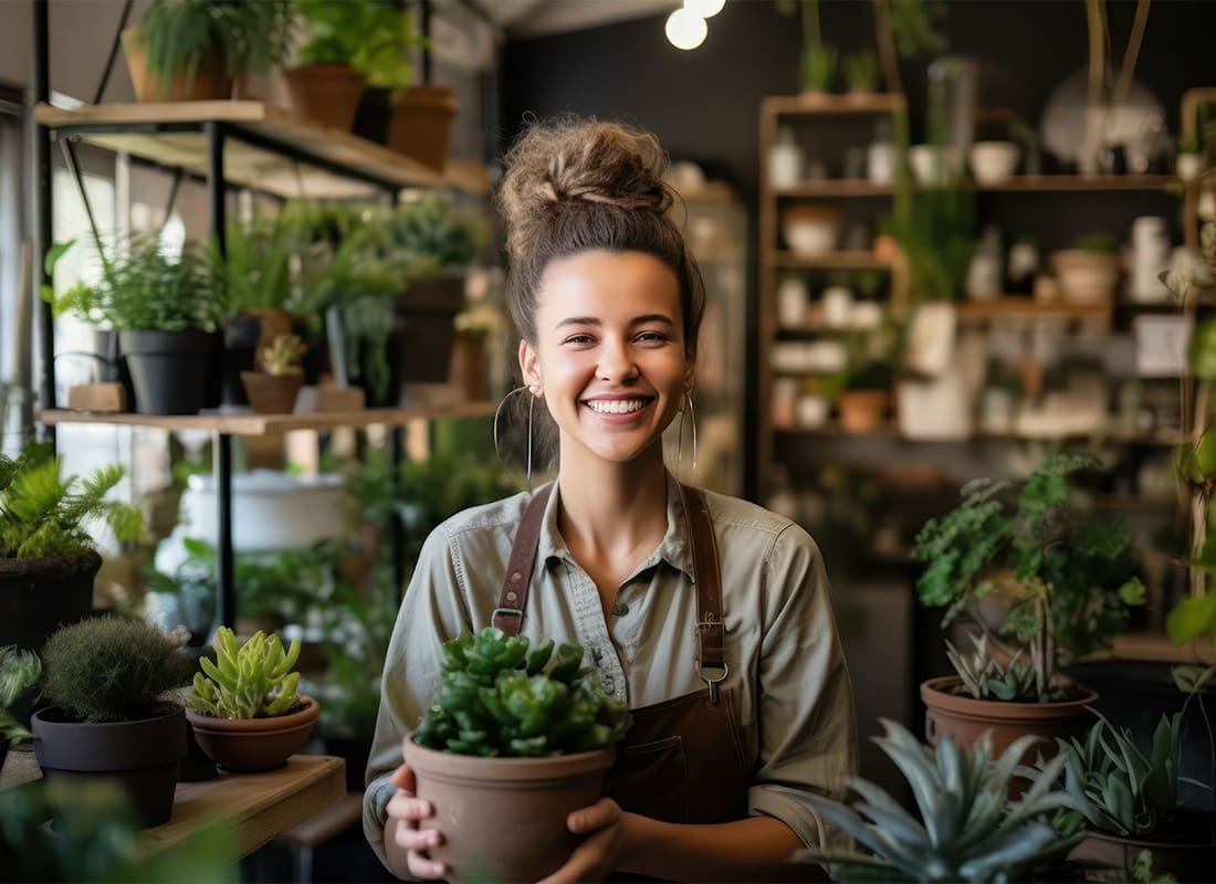 Commercial Insurance - Smiling Portrait of a Young Female Florist Holding a Plant in her Hands While Standing in her Small Flower Shop