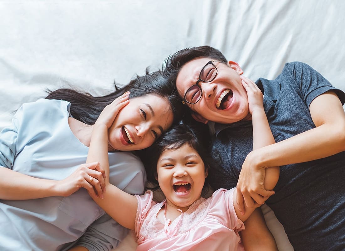 Personal Insurance - Portrait of a Cheerful Asian Family with a Young Daughter Laying in Bed